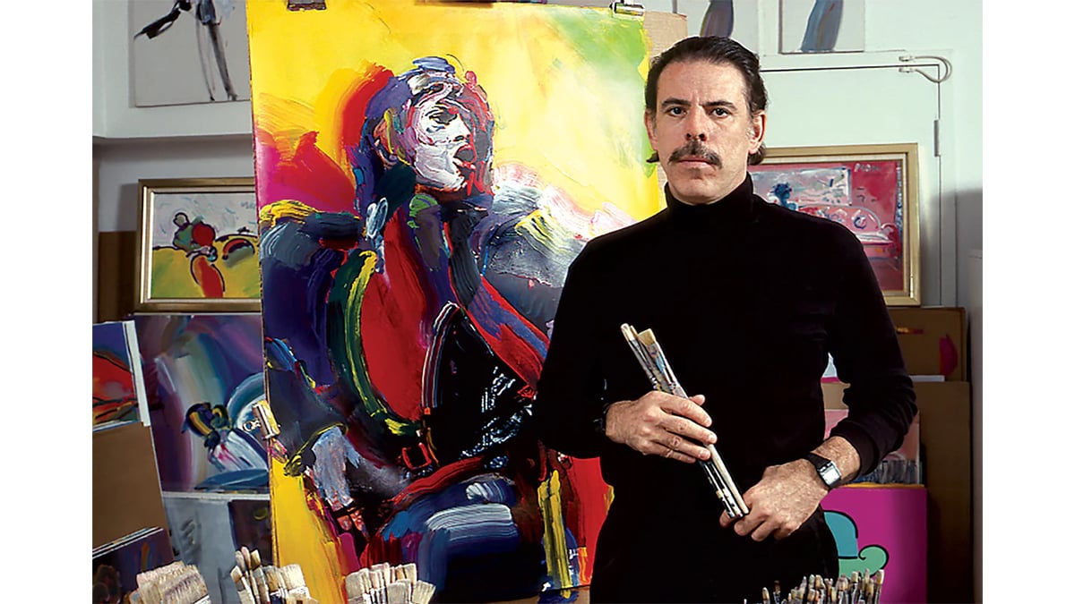 Peter Max standing seeing at the viewer next to his psychedelic art