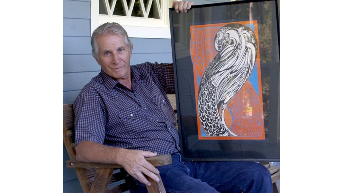 Wes Wilson in a sitting position holding his art in his left land on his left lap