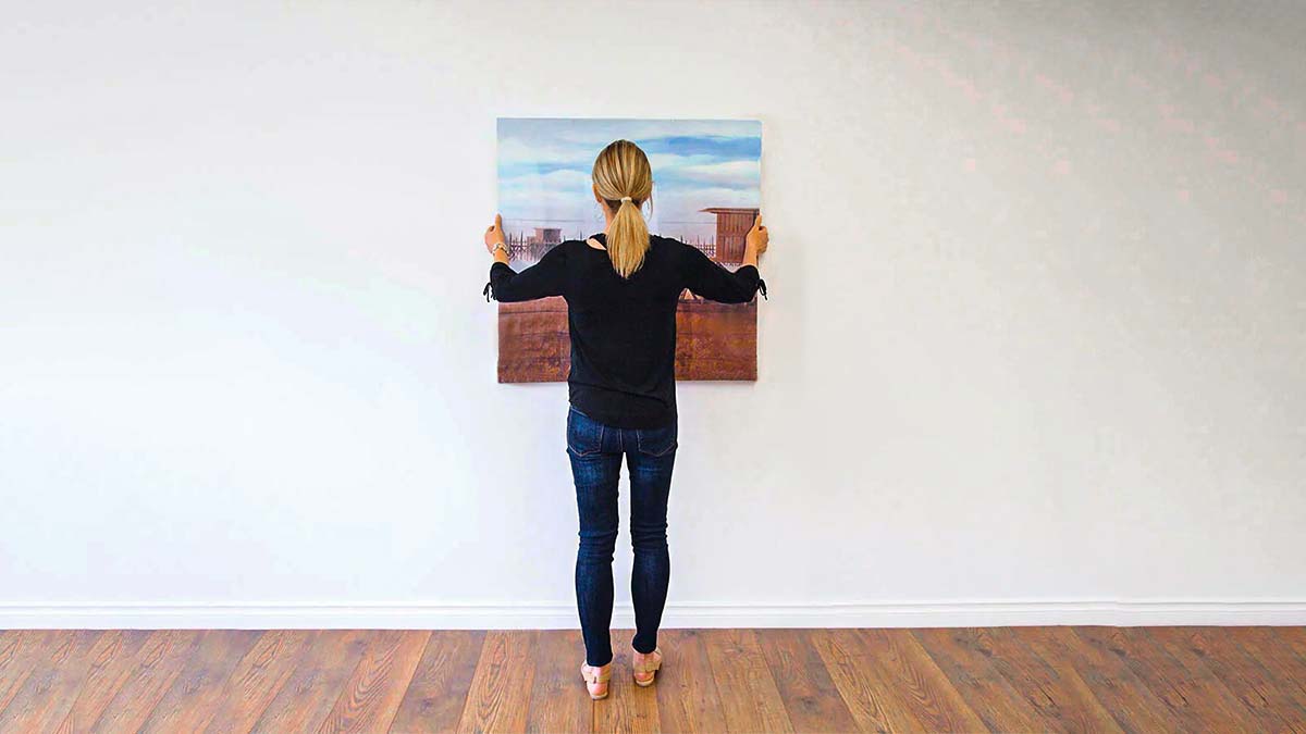 a woman hanging painting on an empty wall with proper placement