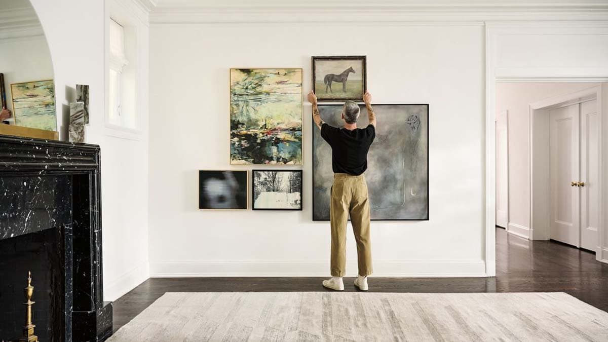 a man hanging a painting with proper wall spacing