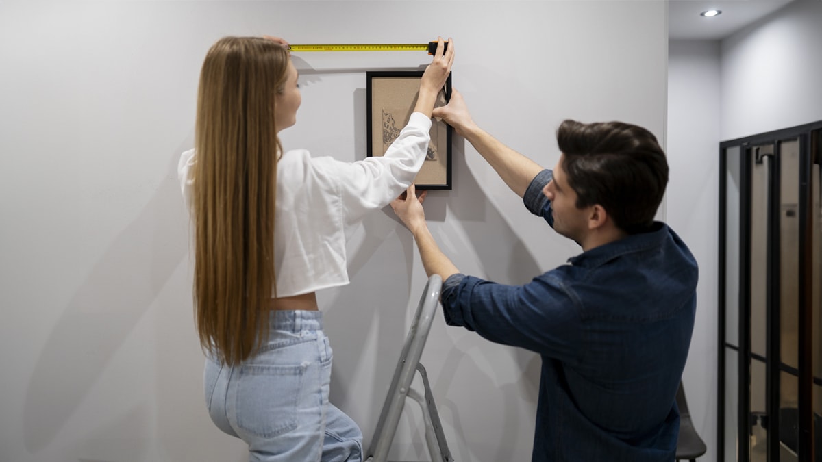 Man and woman measuring painting's height on wall