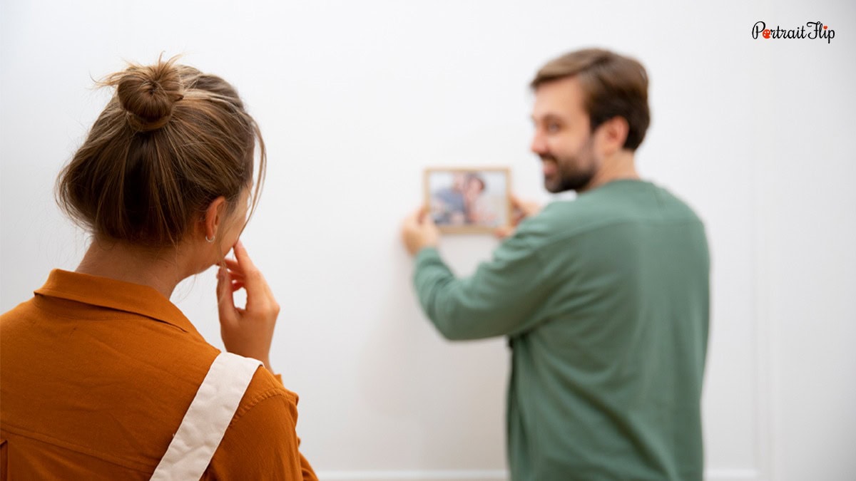 A woman watching a man hanging the frame