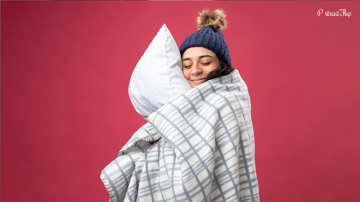 A woman hugging a pillow and covered in throw blanket