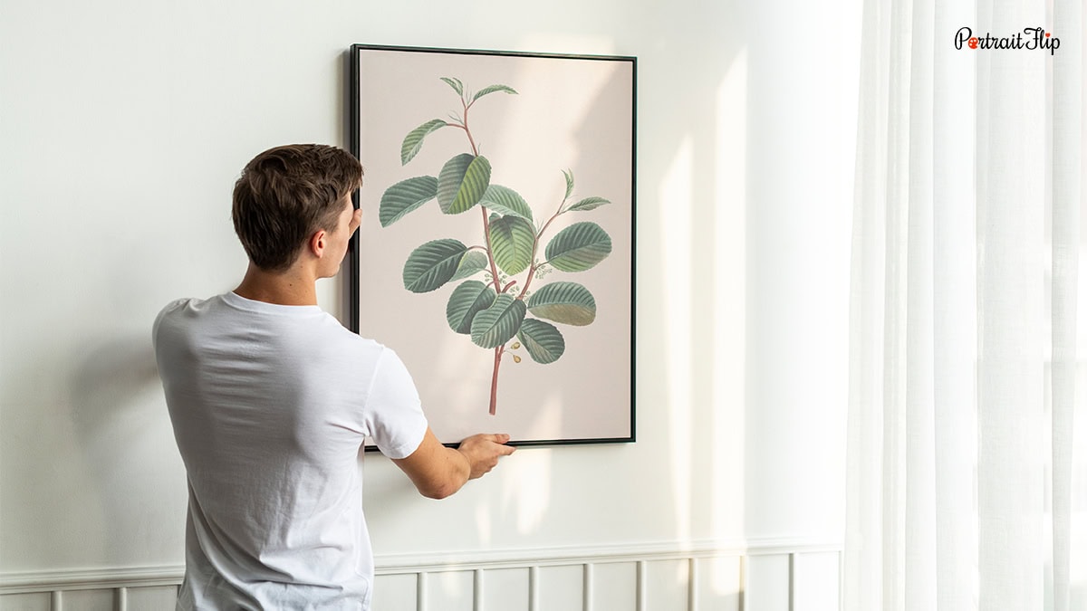A man hanging aplant frame on wall