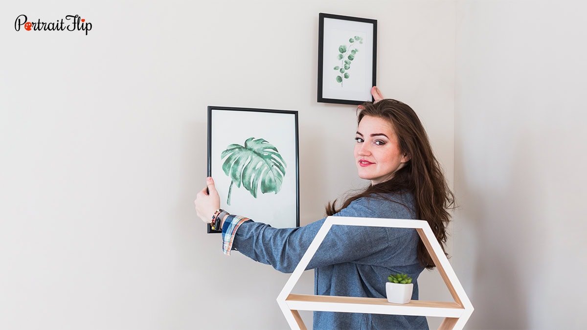 A woman hanging plant photo frames on the wall