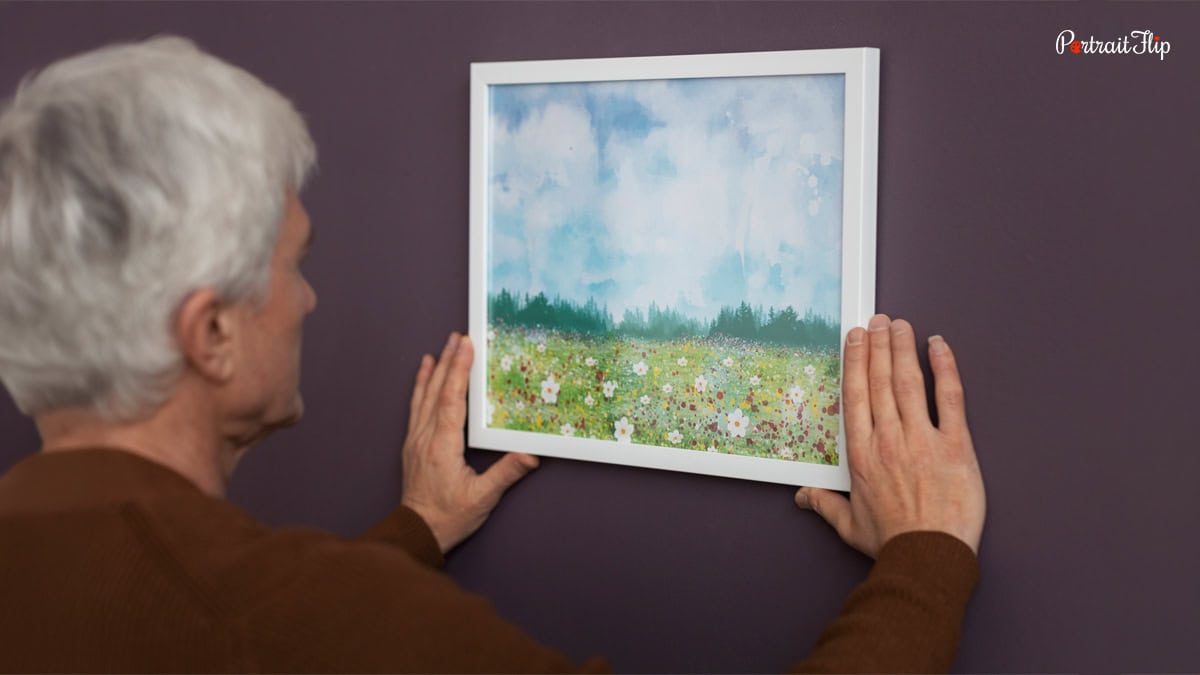 An old man hanging painting on the wall